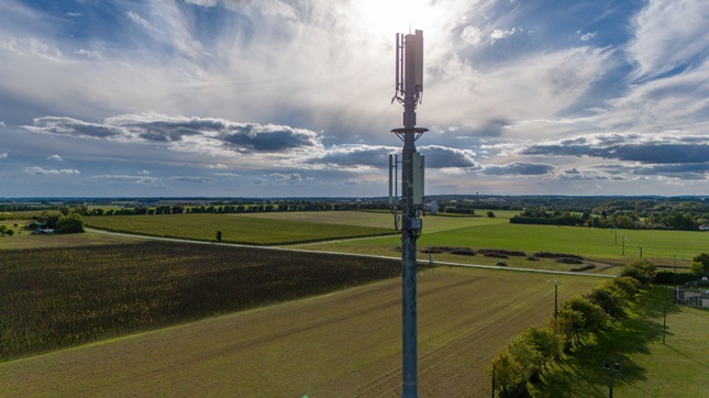 Funkmast in ländlicher Feldlandschaft unter weitem, bewölktem Himmel